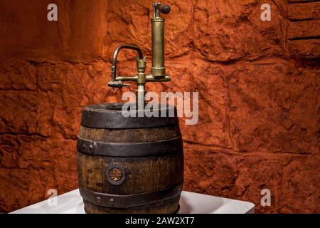 Ein hölzernes Weinfass mit Metallkonstruktion, das auf dem Tisch gegen eine ziegelbraune Wand steht. Stockfoto