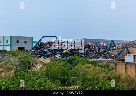 Viele Kräne laden Metallschrott an der großen Müllkippe auf dem Hintergrund eines blauen Himmels. Stockfoto