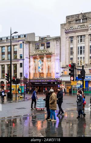 Pendler und Touristen an der Kreuzung von Tottenham Court Road und Oxford Street an einem regnerischen Winternachmittag, London, Großbritannien Stockfoto