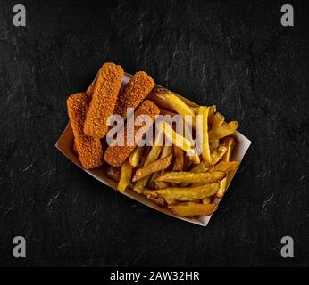 Pommes frites und Nuggets in Papierbox auf schwarzem Hintergrund Stockfoto