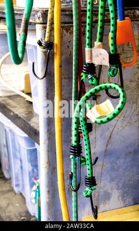 Mehrere verschiedenfarbige Bungeeschnüre hängen vom Dach eines Schuppen. Stockfoto