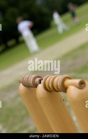 Nahaufnahme von zwei gut abgenutzten Bails auf der Durchgangsgroove von drei Cricket-Baumstümpfe auf einem grünen Grassy Cricket-Platz mit Spielern im Hintergrund unterstützt Stockfoto