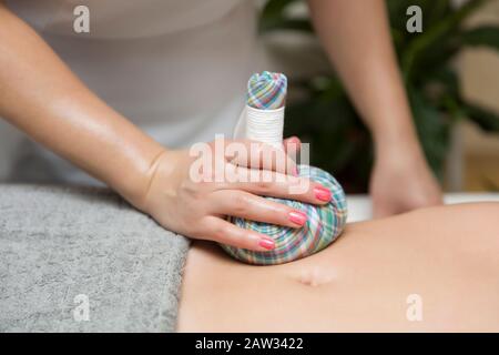 Frau, die im Kosmetiksalon eine Bauchmassage mit aromatischen Kräutertüten hat Stockfoto