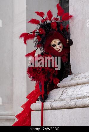 Frau in Maske und verziertes rotes und schwarzes Kostüm, das in San Giorgio steht, fotografiert während des jährlichen Karnevals in Venedig Italien Stockfoto