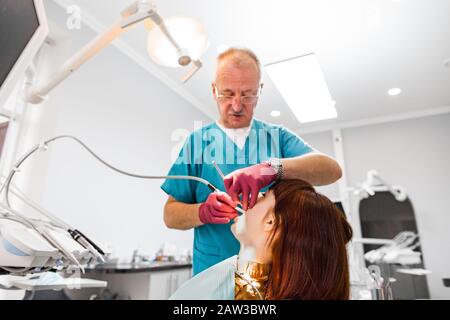 Leitender männlicher Zahnarzt, der mit seiner jungen Patientin arbeitet, die einen Zahnarztbesuch abstattet und in der Klinik eine zahnärztliche Untersuchung und Behandlung hat. Zahnarztberuf Stockfoto