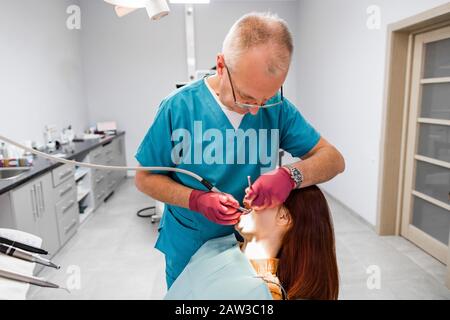 Portrait des Chefarztzahnarztes mit blauer Uniform und Handschuhen, der die Zähne des jungen Fraupatienten in der modernen leichten Zahnmedizin behandelt Stockfoto