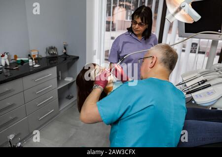 Weibliche Patientin mit offenem Mund während der Bohrbehandlung beim Zahnarzt. Professioneller Zahnmannschaftsmann und Frau, die für junge Frau behandelt werden Stockfoto