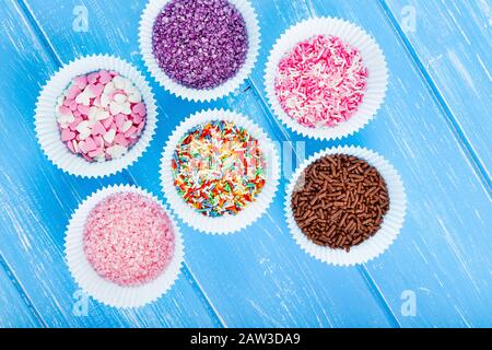 Bunte Süßigkeiten bestreuen den Papierkuchenhalter. Blauer Holzhintergrund im Landhausstil. Stockfoto