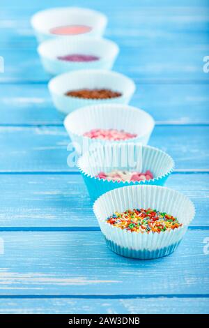 Bunte Süßigkeiten bestreuen den Papierkuchenhalter. Blauer Holzhintergrund im Landhausstil. Stockfoto