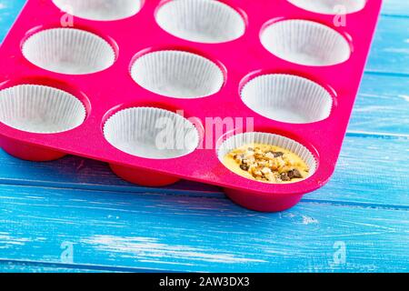 Kuchen in Silikonform auf blauem rustikalem Holzhintergrund gießen. Stockfoto