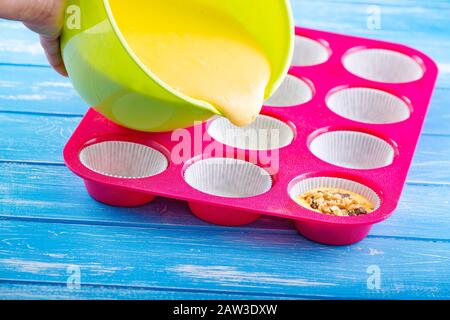 Kuchen in Silikonform auf blauem rustikalem Holzhintergrund gießen. Stockfoto