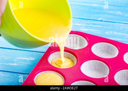 Kuchen in Silikonform auf blauem rustikalem Holzhintergrund gießen. Stockfoto