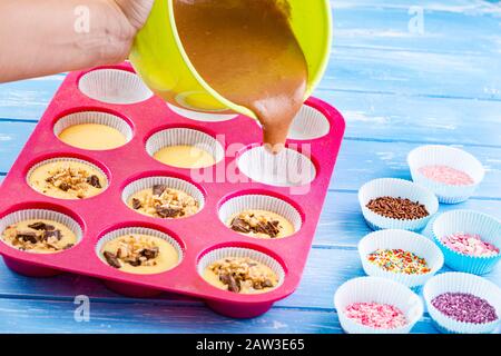 Kuchen in Silikonform auf blauem rustikalem Holzhintergrund gießen. Stockfoto