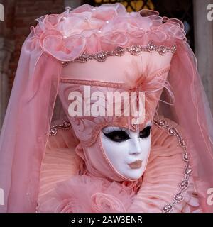 Nahaufnahme der Frau in dekorierter Maske und verziertem rosafarbenem Kostüm, das während des Karnevals in Venedig, Italien, für die Kamera auf dem Markusplatz posiert Stockfoto