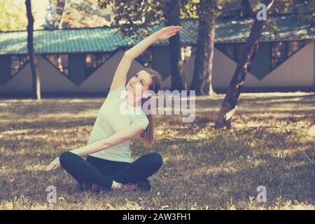 Schöne junge Frau, die auf grünem Gras im Park Dehnübungen macht. Yoga-Workout. Stockfoto