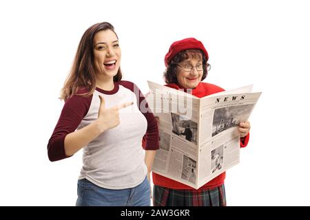 Junge Frauen lachen und zeigen auf eine ältere Frau, die eine Zeitung liest, die auf weißem Hintergrund isoliert ist Stockfoto