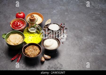 Satz verschiedener Soßen. Beliebte Soßen in Schüsseln - Ketchup, Senf, Mayonnaise auf dunklem Steintisch. Mit Kopierbereich Stockfoto