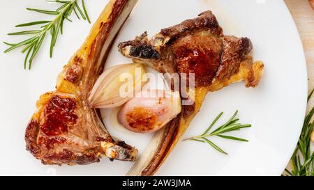 Gebratene Lammrippen auf weißem Teller mit Gemüse und Würze auf weißem Marmortisch, Draufsicht, Langbannerformat Stockfoto