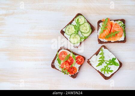 Smorrebrod: Traditionelle dänische Sandwiches. Schwarzes Roggenbrot mit Lachs, Frischkäse, Gurke, Tomaten auf Holzgrund Stockfoto