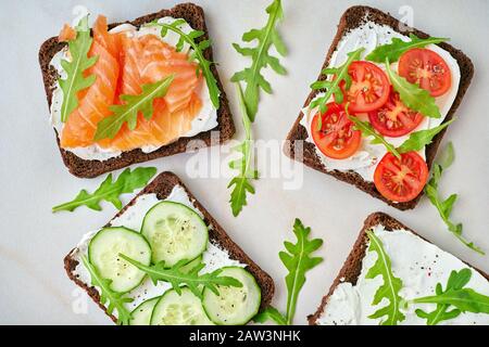 Smorrebrod: Traditionelle dänische Sandwiches. Schwarzes Roggenbrot mit Lachs, Frischkäse, Gurke, Tomaten auf Holzgrund Stockfoto