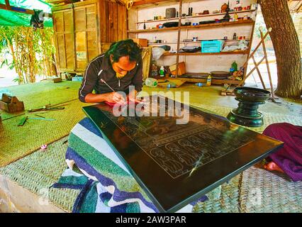 Bagan, MYANMAR - 25. FEBRUAR 2018: Der Handwerker der örtlichen Lackierwerkstatt kratzt die Lackplatte mit Ätznadel, um ein Bild zu machen, Stockfoto