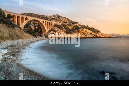 Lange Exposition des Sonnenuntergang in der Calanque des Eaux Salees oder des Salzwassereinlaufs mit Kieselstrand und alter Eisenbahnbrücke in der Nähe von Marseille France Stockfoto