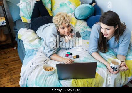 Ein hoher Blickwinkel auf Freunde, die einen Laptop benutzen, während sie zu Hause auf dem Bett liegen Stockfoto