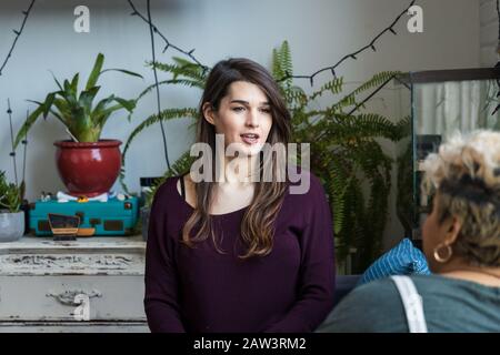 Junge Frau spricht mit Mitbewohnerin, während sie zu Hause im Wohnzimmer sitzt Stockfoto