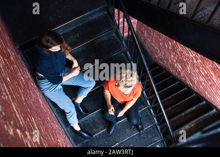 Ein hoher Blickwinkel auf weibliche Freunde, die miteinander auf Schritten zu Hause sitzen Stockfoto