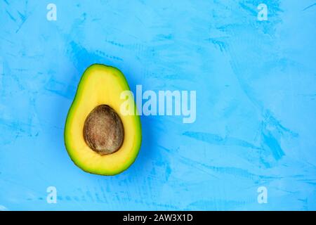 Avocado halbiert, eine Scheibe mit Kern auf einer hellen türkisfarbenen Oberfläche, Nahaufnahme. Köstliche und nahrhafte Früchte, Bild mit Kopierraum. Stockfoto