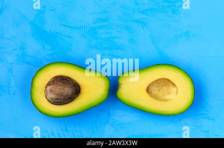 Avocado halbiert, eine Scheibe mit Kern auf einer hellen türkisfarbenen Oberfläche, Nahaufnahme. Köstliche und nahrhafte Früchte, Bild mit Kopierraum. Stockfoto