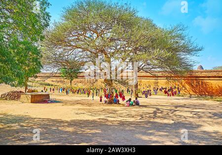 Bagan, MYANMAR - 25. FEBRUAR 2018: Der ausgebreitete schattige Baum mit zahlreichen hängenden Streichelpuppen von Marktstall an der Wand der Dhammayangyi-Pagode, an Stockfoto