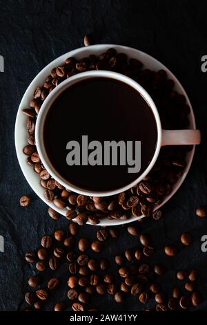 Eine weiße Tasse mit schwarz duftendem Kaffee steht auf schwarzem Grund Stockfoto