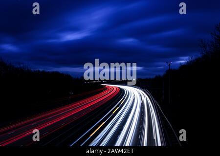 Die Autobahn M1, die mit einer langsamen Shutterspeed fährt, bietet an einem stürmischen Winterabend fantastische bunte Lichtwege. Stockfoto