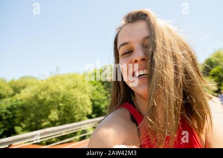 Porträt einer lachenden jungen Frau mit unordentlichen Haaren wegen des Windes an einem sonnigen Tag. Genuss in der Natur Stockfoto