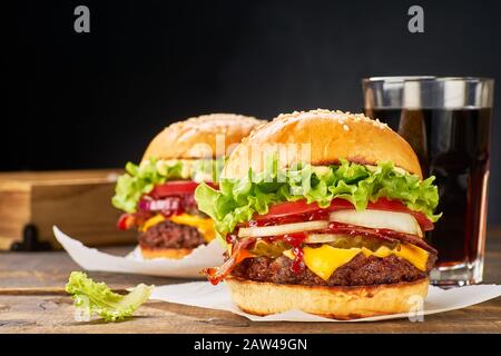 Köstliche Hamburger und ein Glas Getränk auf dunklem Holztisch. Fast-Food-Konzept Stockfoto