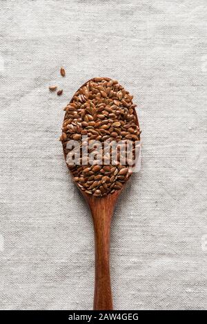 Flachssamen in einem Holzlöffel auf einem natürlichen Leinentisch. Vertikales Format. Nahaufnahme. Stockfoto