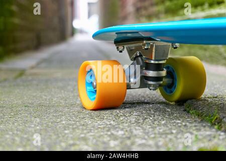 Vor blauem Mini-Cruiserpenny-Brett aus Kunststoff oder Skateboard mit gelben und orangefarbenen Rädern auf Betonfliesen in einer Gasse mit Licht am Ende Stockfoto