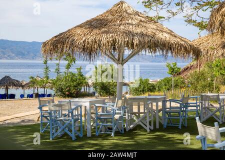 Palapa Schattiertische und Stühle am Strand von Vlichos auf der Insel Hydra, einer der Saronischen Inseln in der ägetischen See. Stockfoto