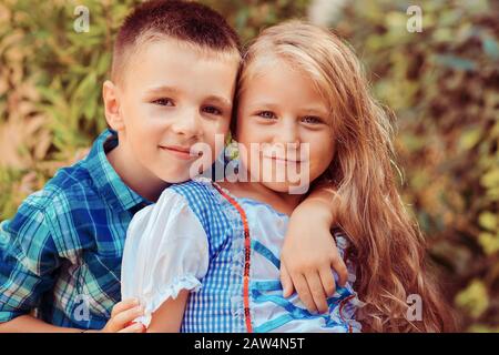 Schwester mit Bruder zeigt Zuneigung, umarmt und lächelt isoliert Natur grünen Strauchbaum Hintergrund Stockfoto