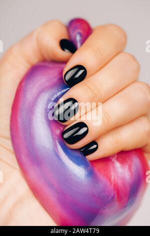 Hände mit schwarzen Maniküre holding Schleim in Blau und Rosa leuchtende Farben Stockfoto