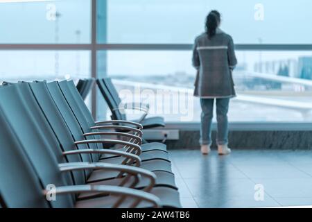 Junge Brunette Curly Woman In Der Nähe Von Big Window Im Modernen Flughafen Wartet Auf Eine Einschiffung In Den Urlaub. Flug verzögert sich Stockfoto