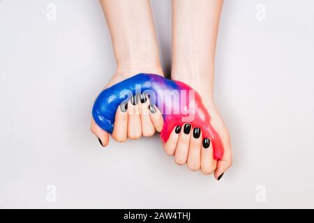 Hände mit schwarzen Maniküre holding Schleim in Blau und Rosa leuchtende Farben Stockfoto