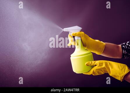 Frau, die gelbe Gummihandschuhe mit grüner Sprühflasche trägt und Flüssignebel in die Luft sprüht, kühler Lichteffekt. Viel Kopierspeicher. Stockfoto