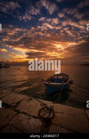 Sonnenuntergang in einem kleinen Hafen von Salento Porto Cesareo mit einem Fischerboot und einem dramatischen Himmel Stockfoto