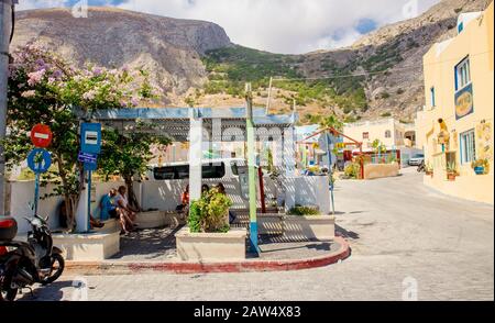 Kamari, Santorini/Griechenland-14Jul2019: Kamari Strandbustop. Touristen sitzen und warten auf den Bus. Berg Mesa vouno im Hintergrund. Stockfoto