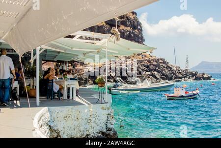 Oia, Santorini/Griechenland 14Jul2019-Ammoudy Bay mit Fischerbooten und Fischtavernen. Touristen verbringen Zeit und essen in traditionellen griechischen Tavernen. Stockfoto