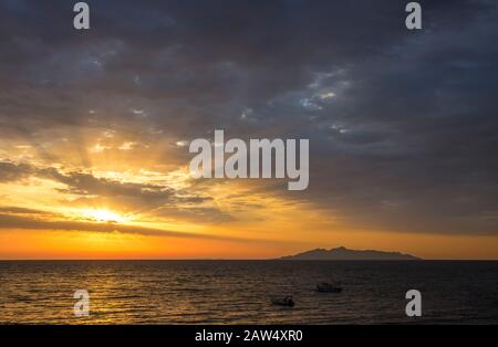 Sonnenaufgang vom ägetischen Meer, magische Sonnenstrahlen, die durch Wolken leuchten, Silhouette der Vulkaninsel (Anafi, Griechenland, von der Insel Santorini aus gesehen) auf dem Bac Stockfoto