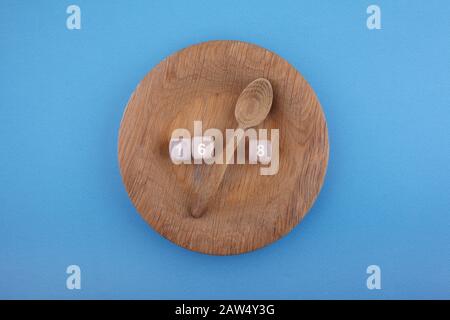 Intermittierendes Fasten. Holzlöffel zwischen Holzwürfel mit den Zahlen 16 und 8 auf dem Teller. Gesundheits- und Fitness-Trend. Stockfoto