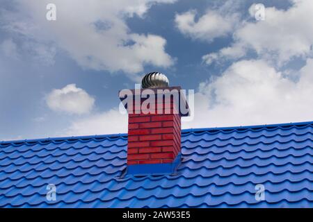 Gegen den Himmel. Ein roter Kamin mit Drehbarem Cowl auf blauem Metalldach. Stockfoto